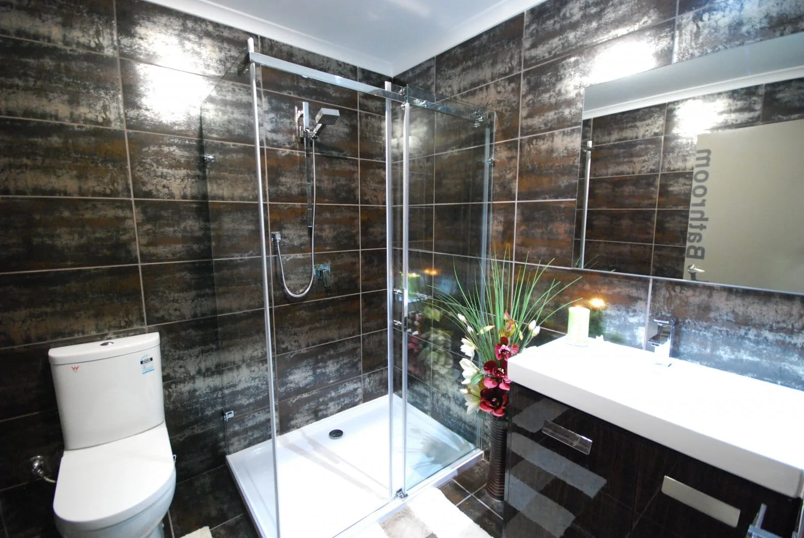 Private shower room with dark metallic tiles, glass shower and floral arrangement