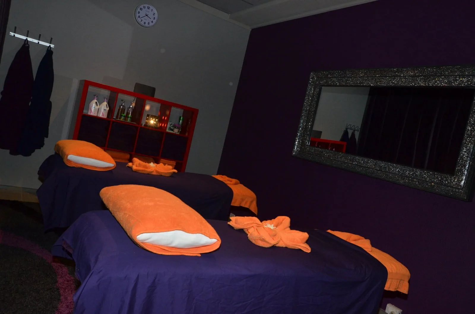 Twin-bed treatment room with purple linen, orange bolster pillows and ornate silver mirror