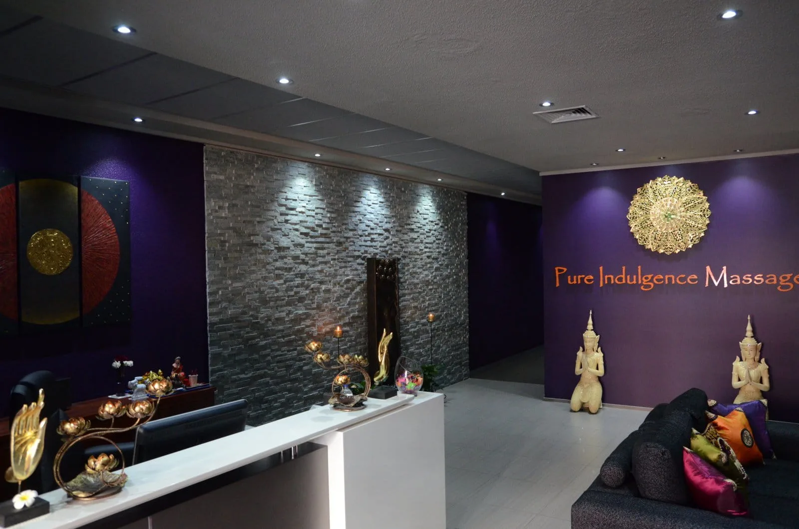 Reception — slate stone feature wall, gold mandala, gilded deva statues and jewel-tone cushions